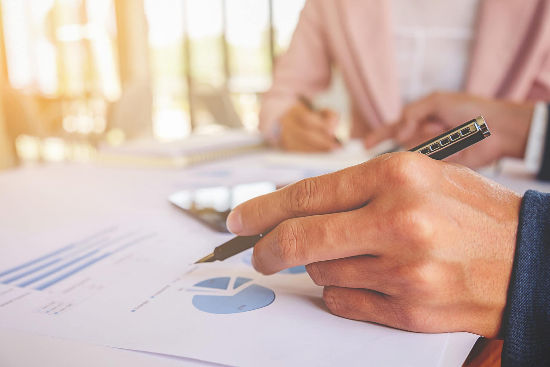 Une main tient un stylo sur un bureau couvert de feuilles