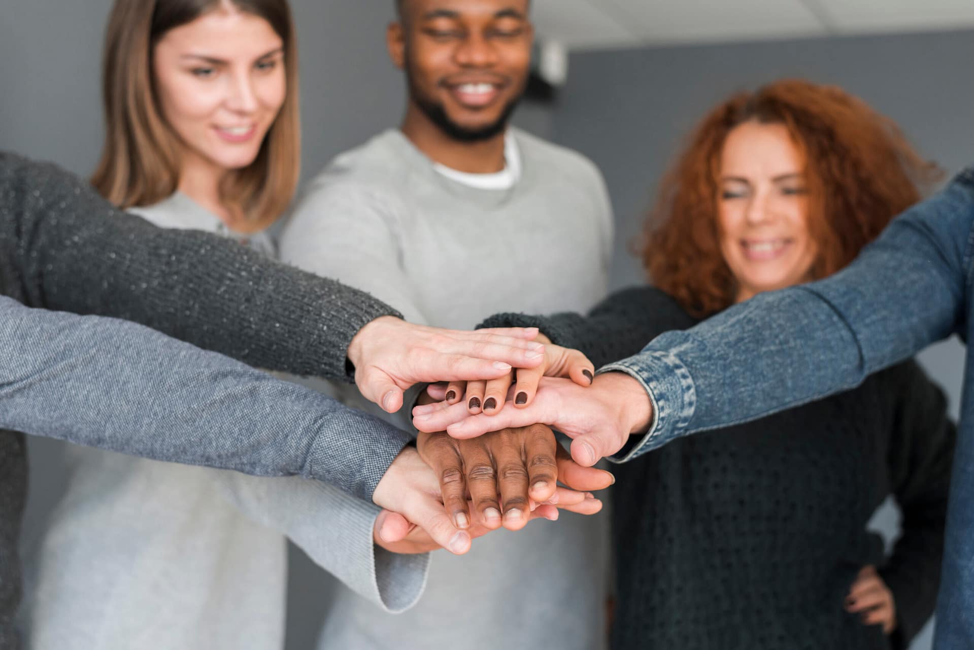 5 personnes empilent en souriant leurs mains droites les unes sur les autres